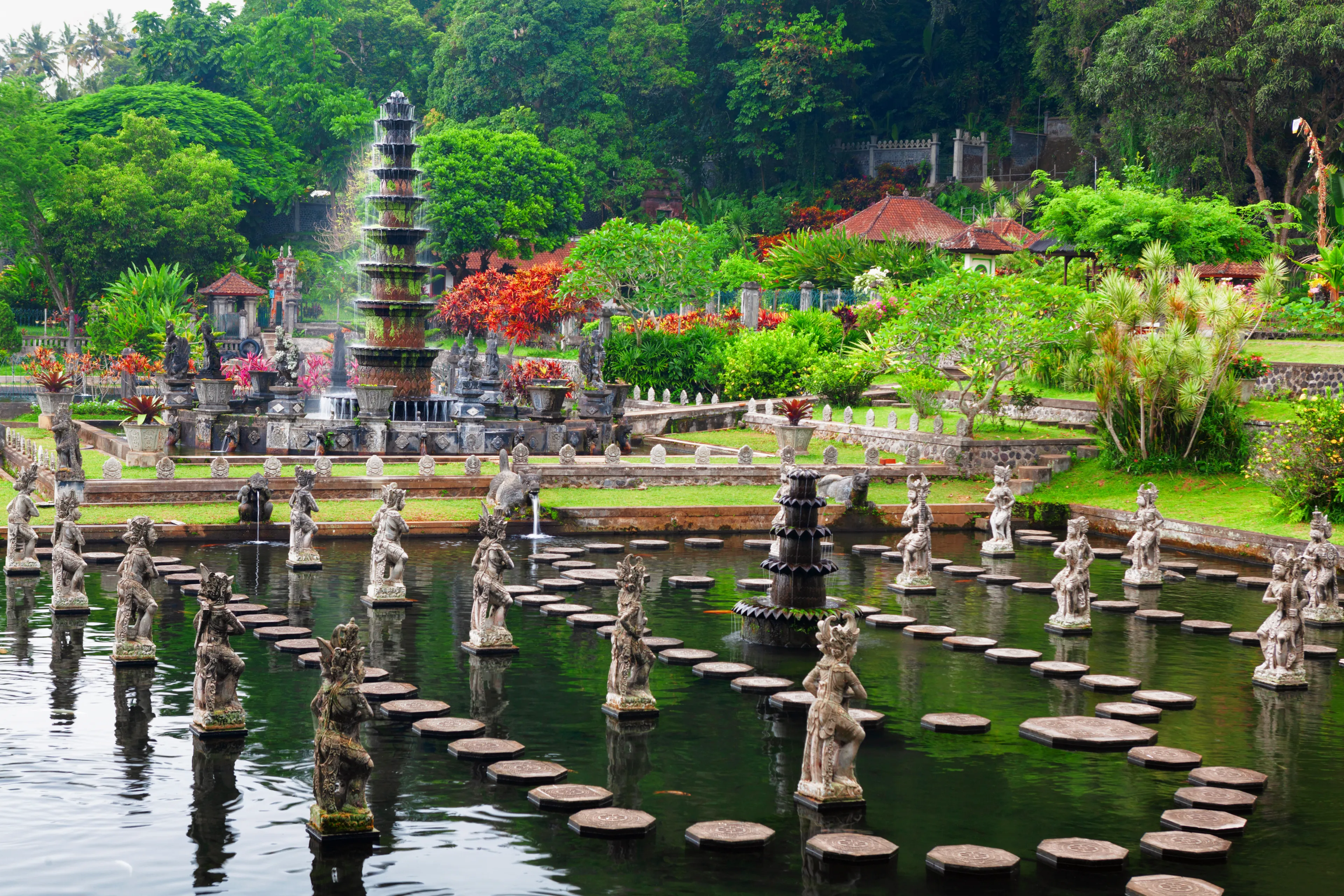 Ancient water palace Tirta Gangga with fountains, natural pools, path in fish pond with statues of dancing women in traditional costumes. Culture, arts of Bali, popular travel destination in Indonesia