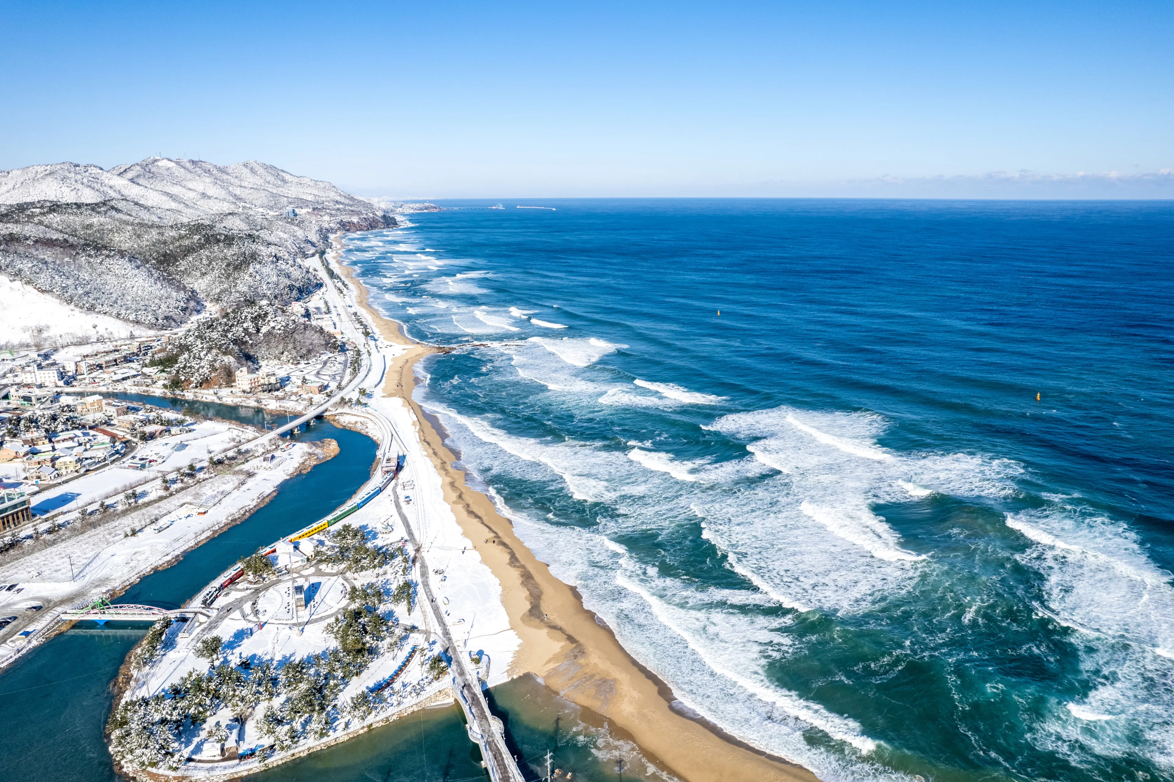 Jeongdongjin, Gangneung-si, Gangwon-do, South Korea - December 26, 2021: Aerial and morning view of of snow covered Jeongdongjin Beach and Station with big waves on the sea 