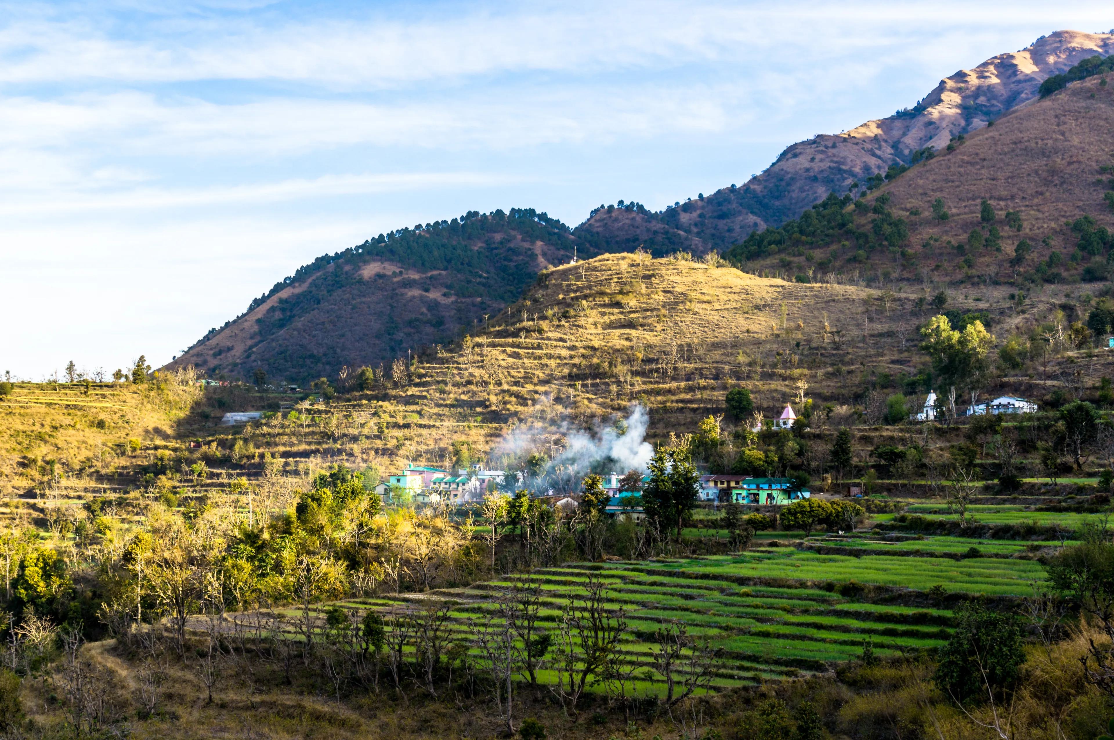 Landscape shot of Dehradun with a village on a hillside. The smoke coming from the village, the grassy stepped fields and beautiful surroundings make this a perfect tourism shot