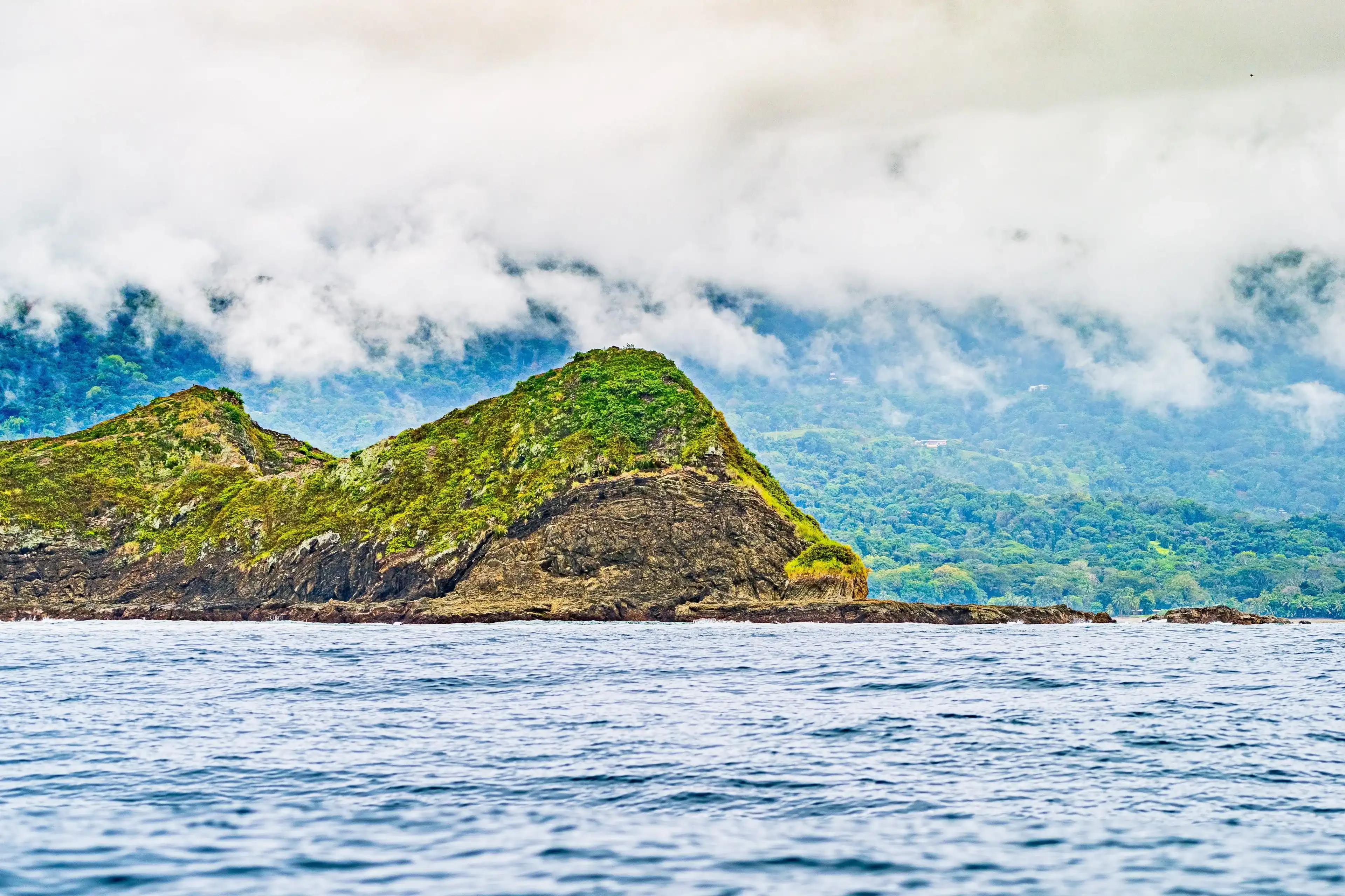 Misty coastal landscape with rugged hills covered in greenery, waves crashing against the rocky shore, and forested mountains in the background. Uvita Puntarenas Province Costa Rica. Pacific Cost. Misty coastal landscape with rugged hills covered in greenery, waves crashing against the rocky shore, and forested mountains in the background. Uvita Puntarenas Province Costa Rica. Pacific Cost.