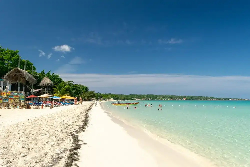 Negril, Jamaica - May 30 2015: People/ tourists at Seven Mile Beach on Westmoreland coast on sunny summer vacation day. Beautiful tropical Caribbean island holiday scene. Rasta color glass bottom boat Negril, Jamaica - May 30 2015: People/ tourists at Seven Mile Beach on Westmoreland coast on sunny summer vacation day. Beautiful tropical Caribbean island holiday scene. Rasta color glass bottom boat