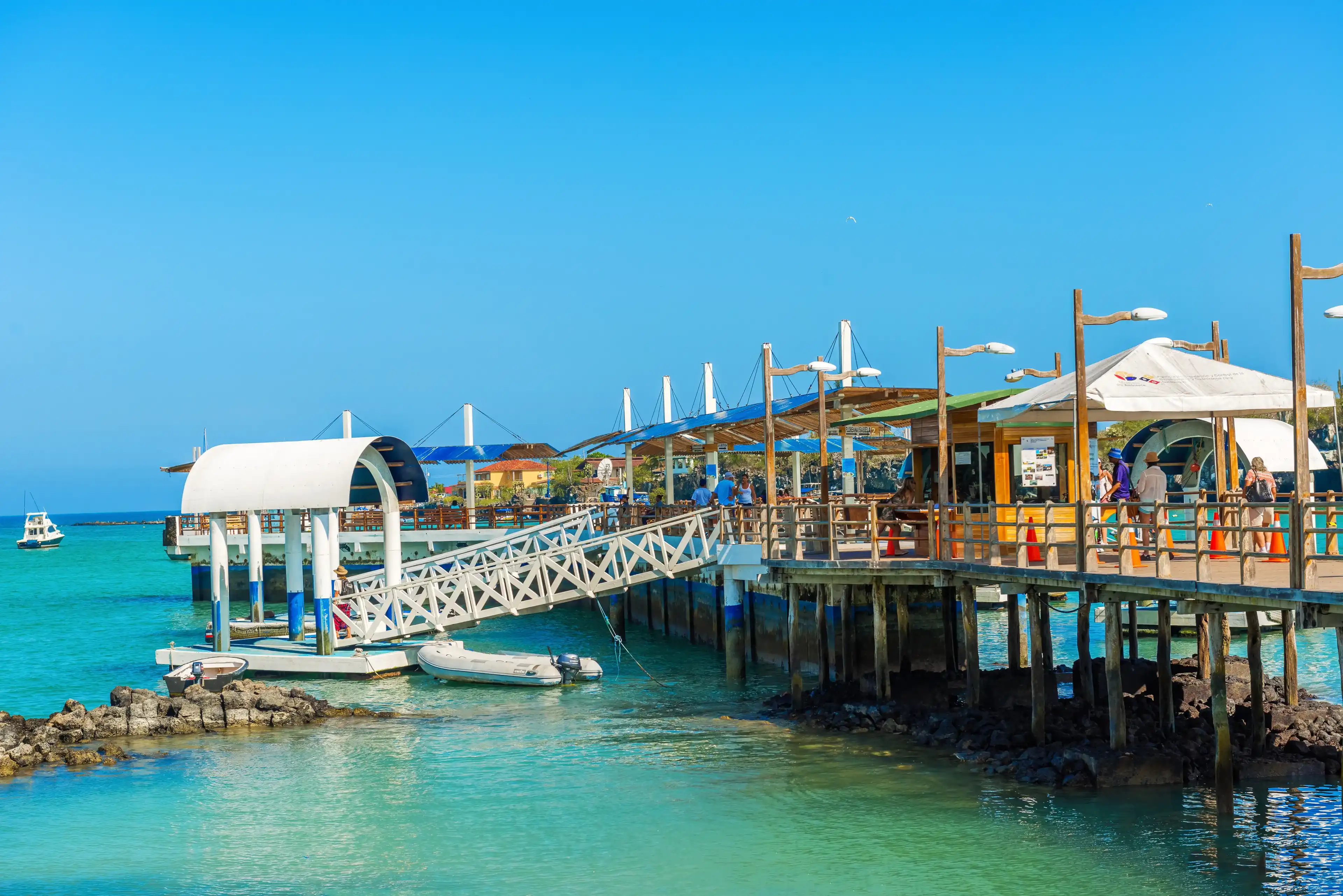 Puerto Ayora, Galapagos, Ecuador - April 1, 2016: People walking and waiting for the boats on the pier in Puerto Ayora in Galapagos on a sunny day. Puerto Ayora, Galapagos, Ecuador - April 1, 2016: People walking and waiting for the boats on the pier in Puerto Ayora in Galapagos on a sunny day.