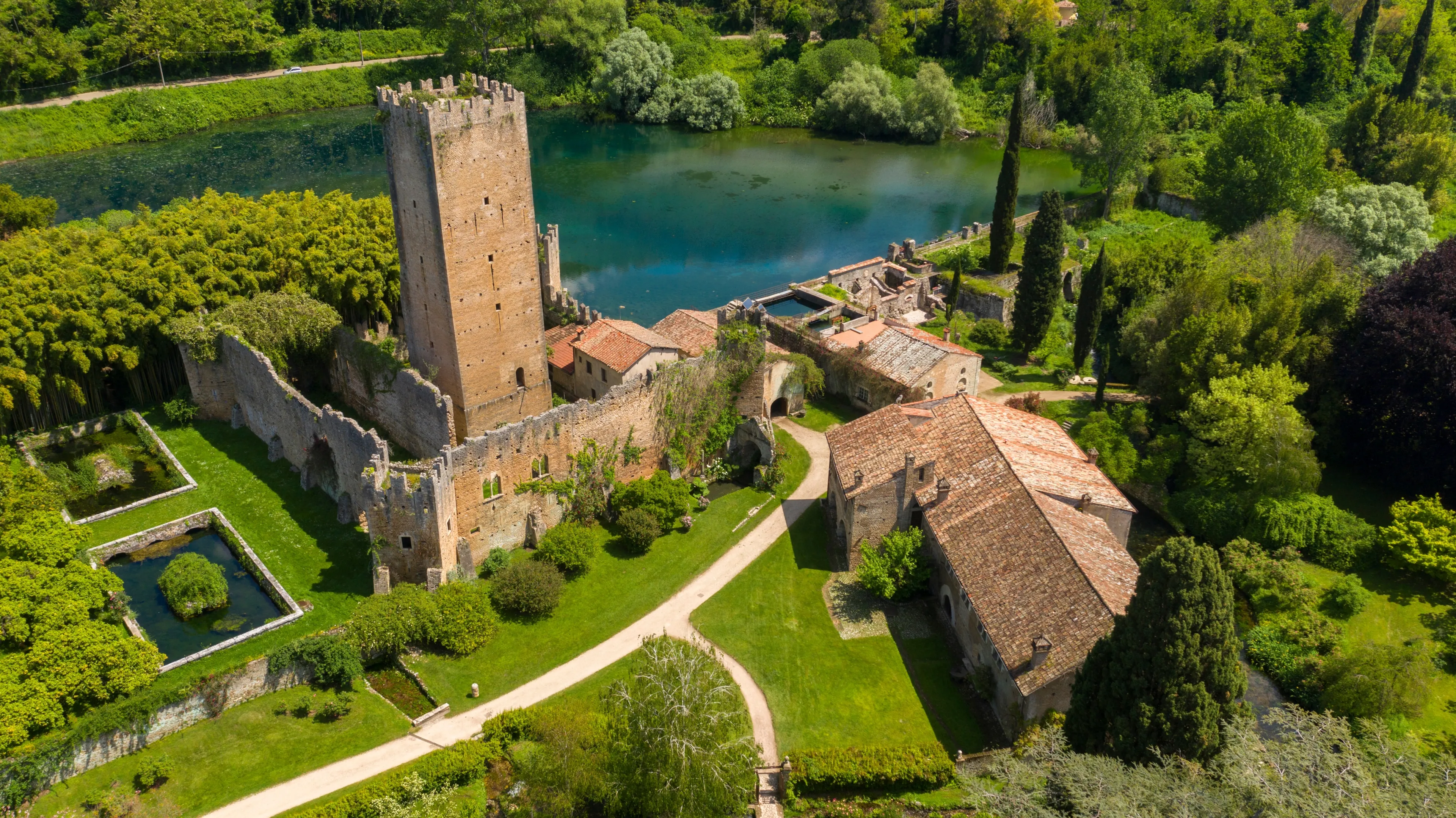 Aerial view of the ruins of the castle and tower located in the garden of Ninfa, near Latina, Italy. The park is an Italian natural monument and contains a lake and a river. It is empty.