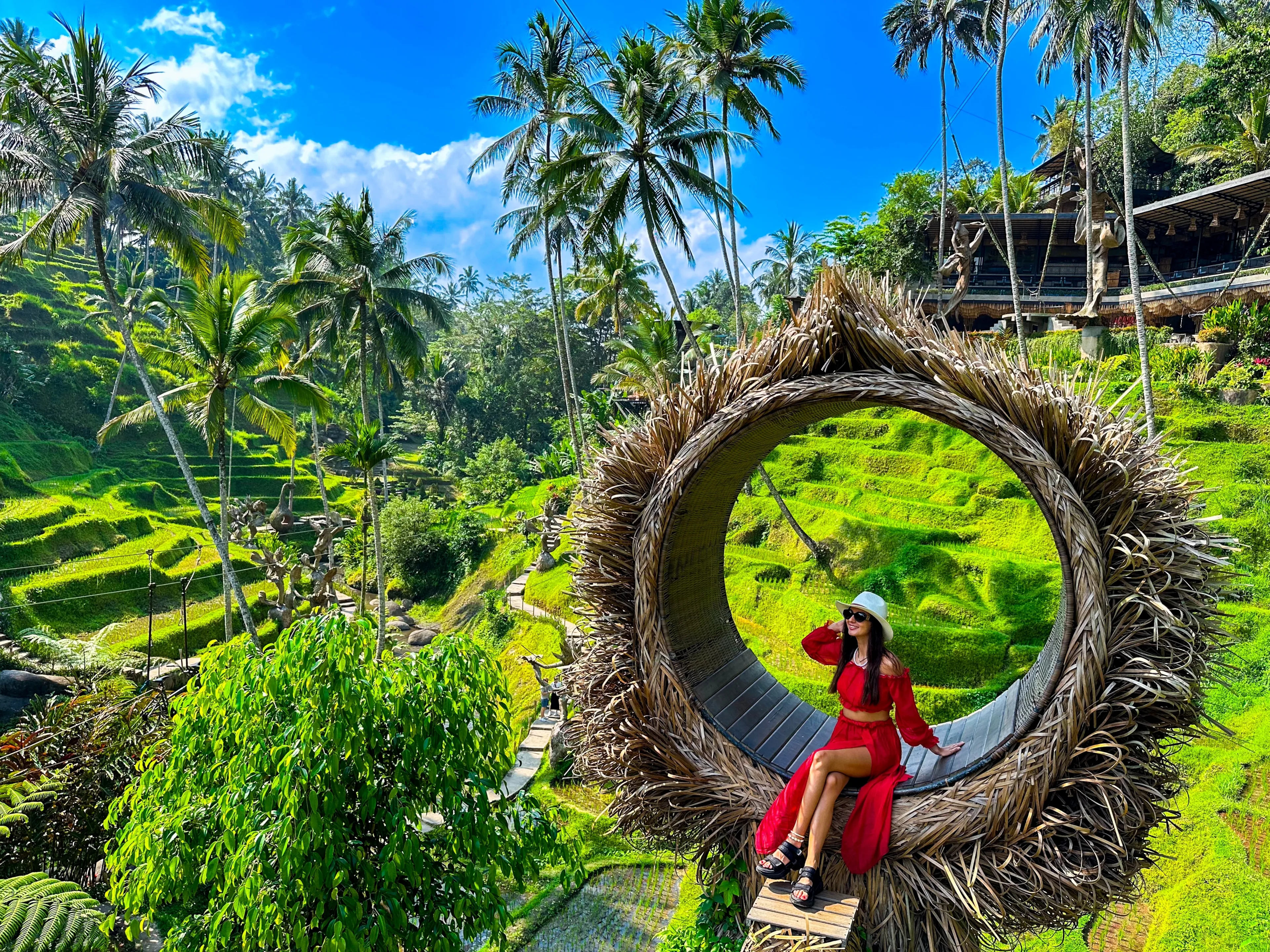 Ceking Rice Terrace (Tegalalang Rice Terrace), Ubud, Bali, Indonesia, October 2023. A stylish girl in a red dress, and a straw hat sitting on the spot view overlooking the tropical paradise