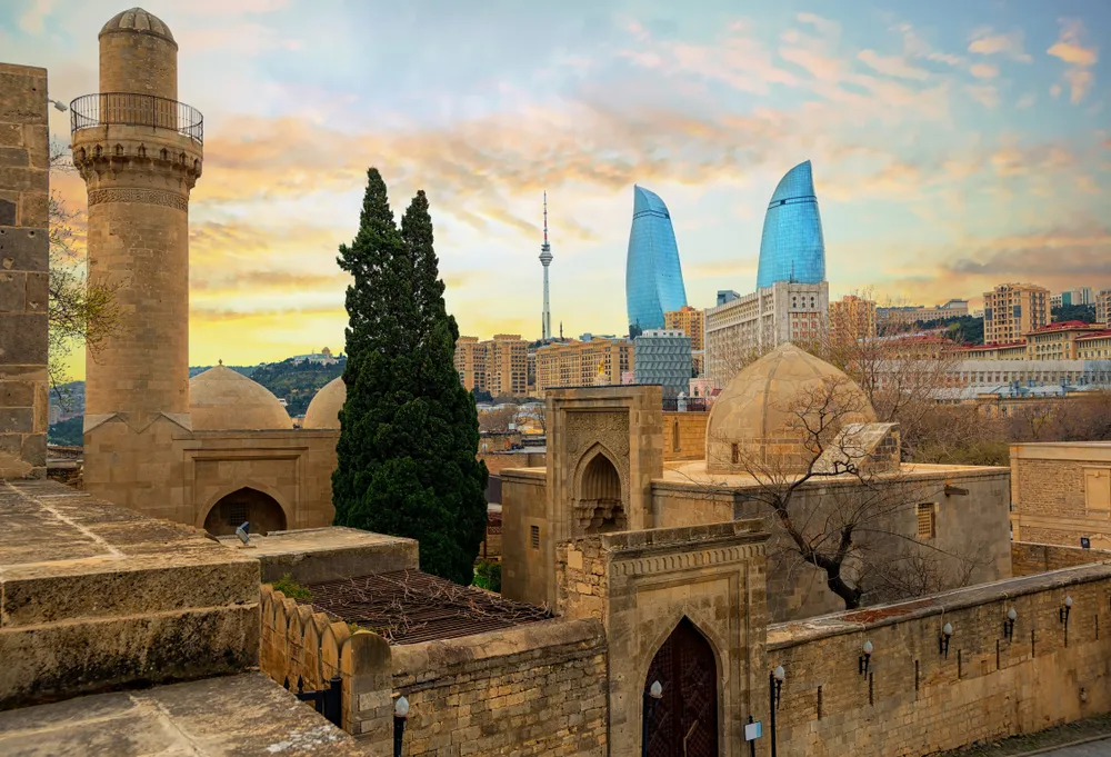 Baku city, Azerbaijan, view of the historical mosques and the walls of Shirvanshahs palace in the Old town and modern glass Flame Towers skyscrapers in dramatic sunset light