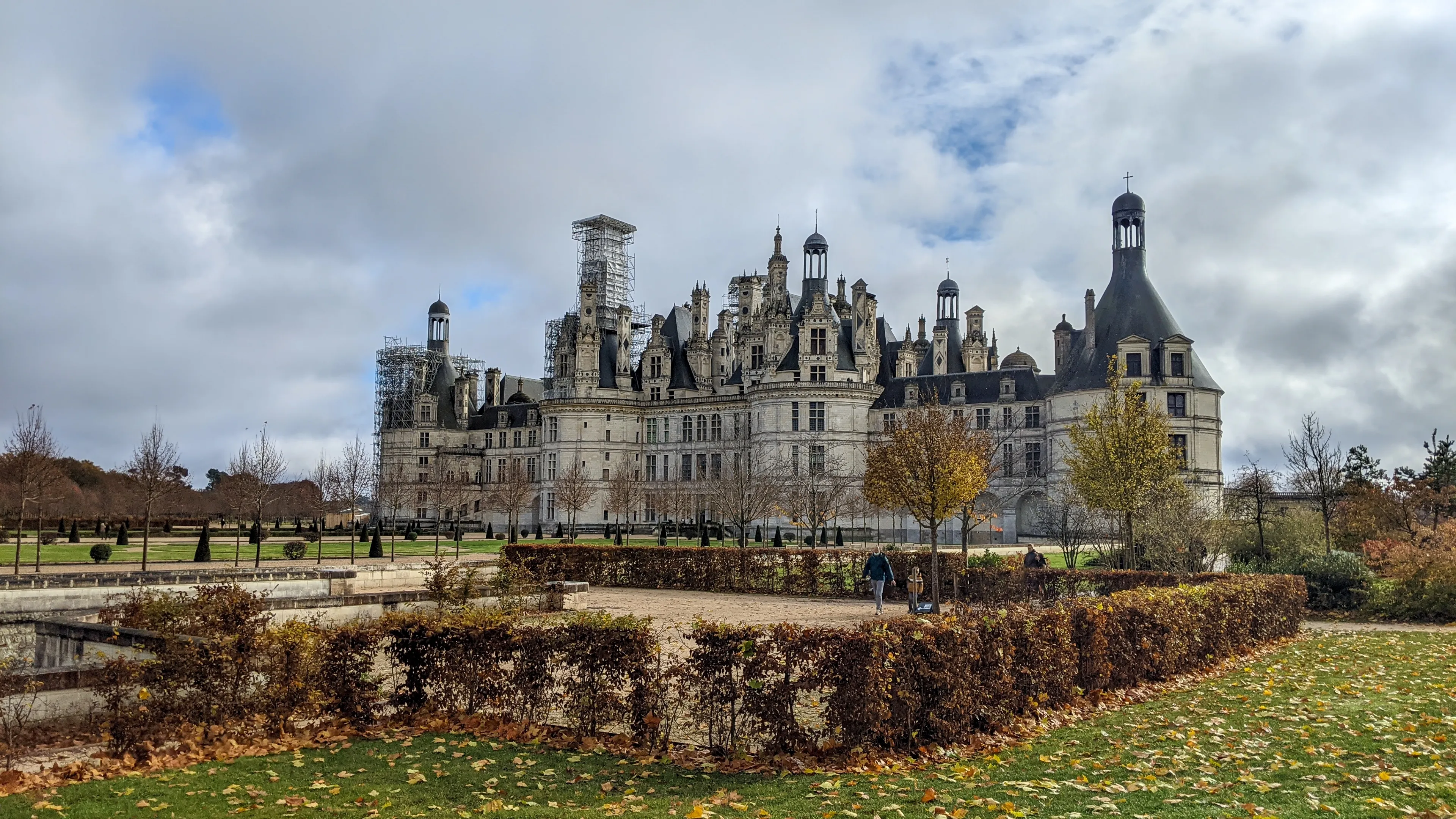 Chambord, Centre-Val de Loire, France, November 15, 2023 - Chateau de Chambord on cloudy autumn day. Renaissance architecture, formal gardens, scaffolding on towers. Tourists visible