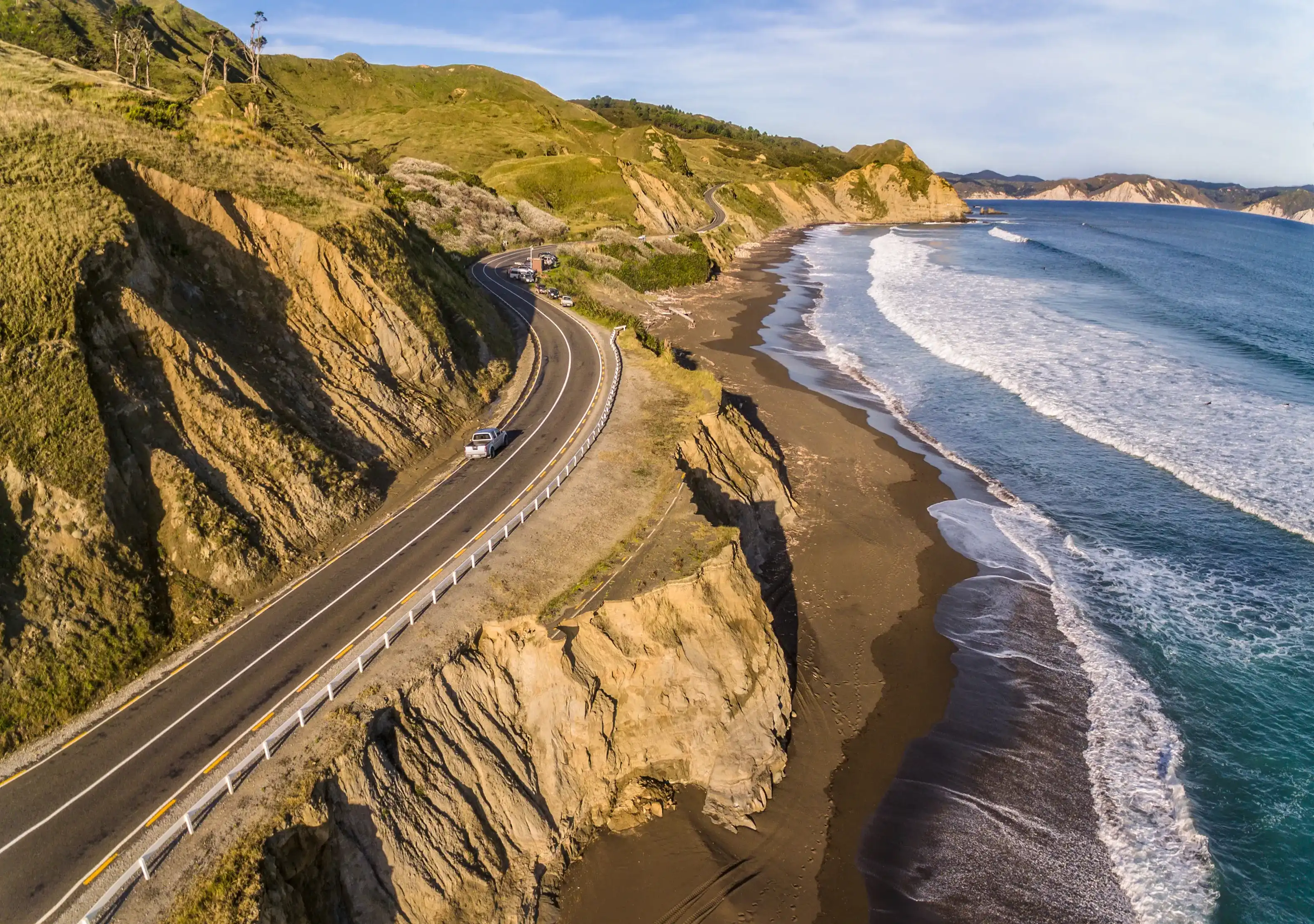 Aerial view of the road leading to Mahia peninsula around ocean. New road next to old damaged asphalt road. Golden hour. North Island of New Zealand. Aerial view of the road leading to Mahia peninsula around ocean. New road next to old damaged asphalt road. Golden hour. North Island of New Zealand.