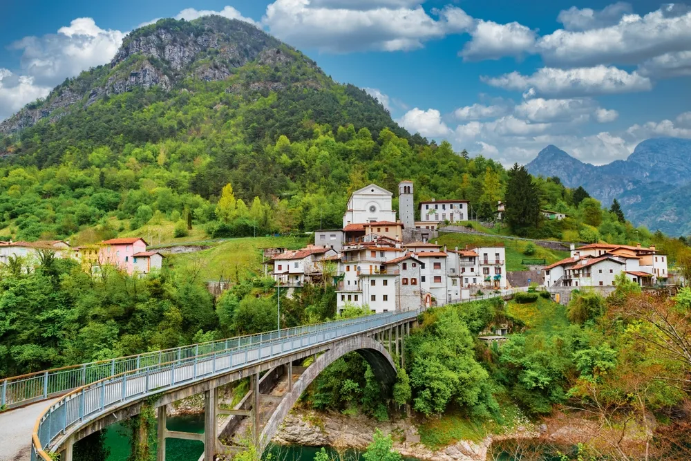 Scenic alpine village in Pordenone, Italy. Arc bridge and old houses on the mountain foot. Chievolis village near Meduno.