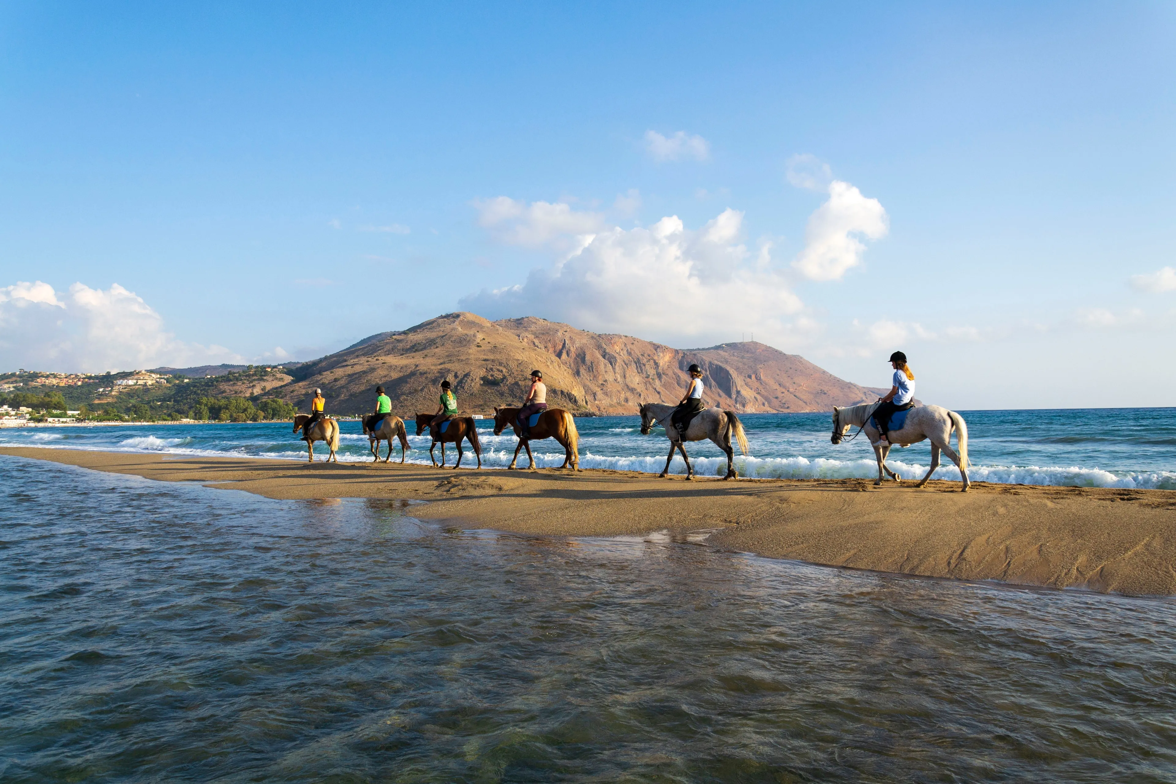 GEORGIOUPOLI, GREECE – AUGUST 8 2022: Young women riding horses on the beach at dawn on August 8, 2022 in Georgioupoli, Greece.