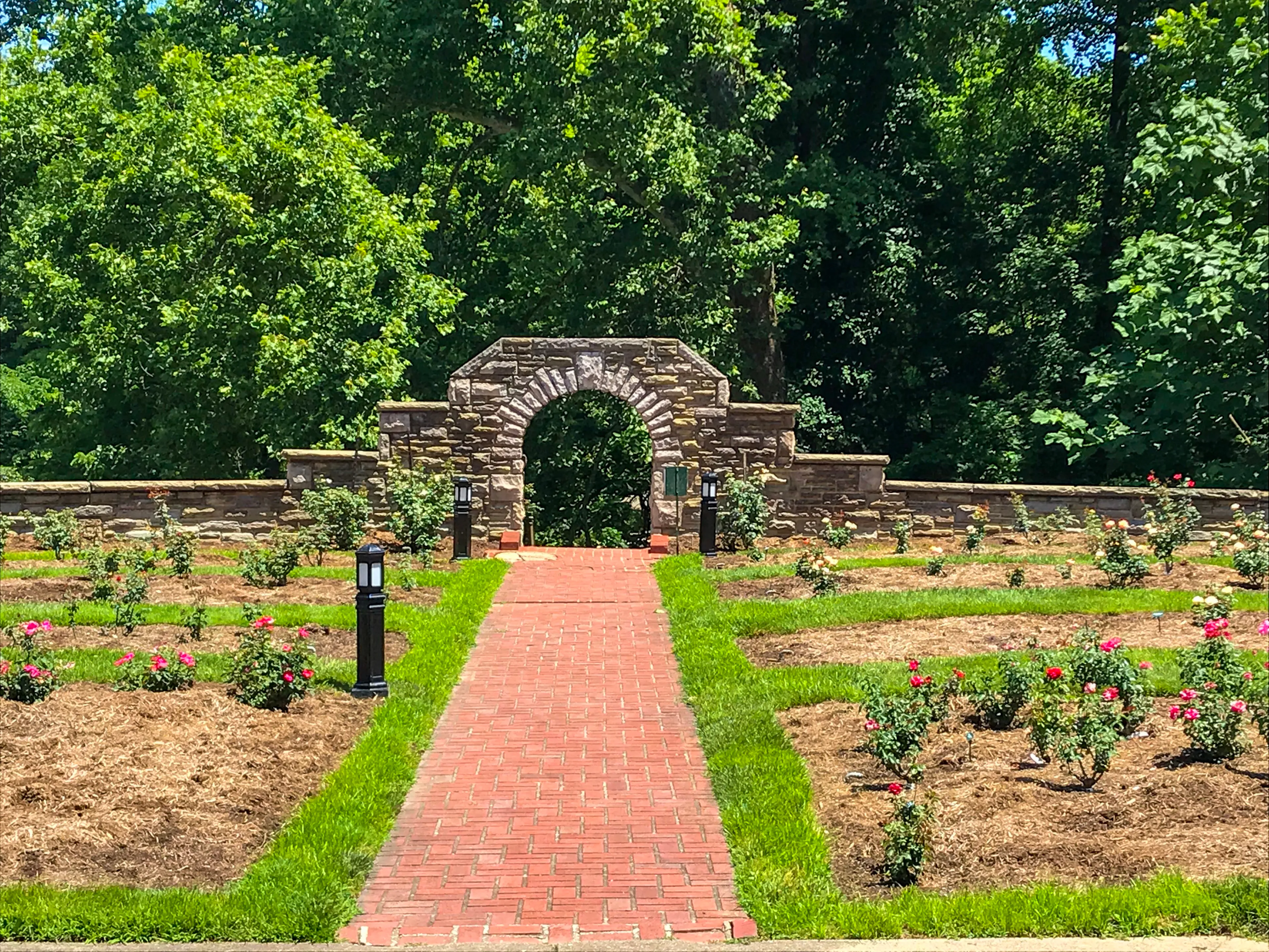Huntington Rose Garden in West Virginia. Stone entrance, red brown bricks leading to the round stone gate. roses on both sides of the pathway.