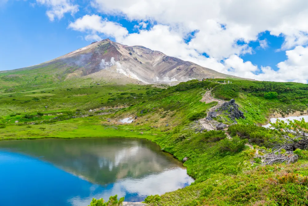 Scenery of Asahidake peak mountain with reflection water and blue cloudy sky in summer, Asahikawa, Hokkaido, Japan. The tallest mountain in Hokkaido and located in the Daisetsuzan National Park