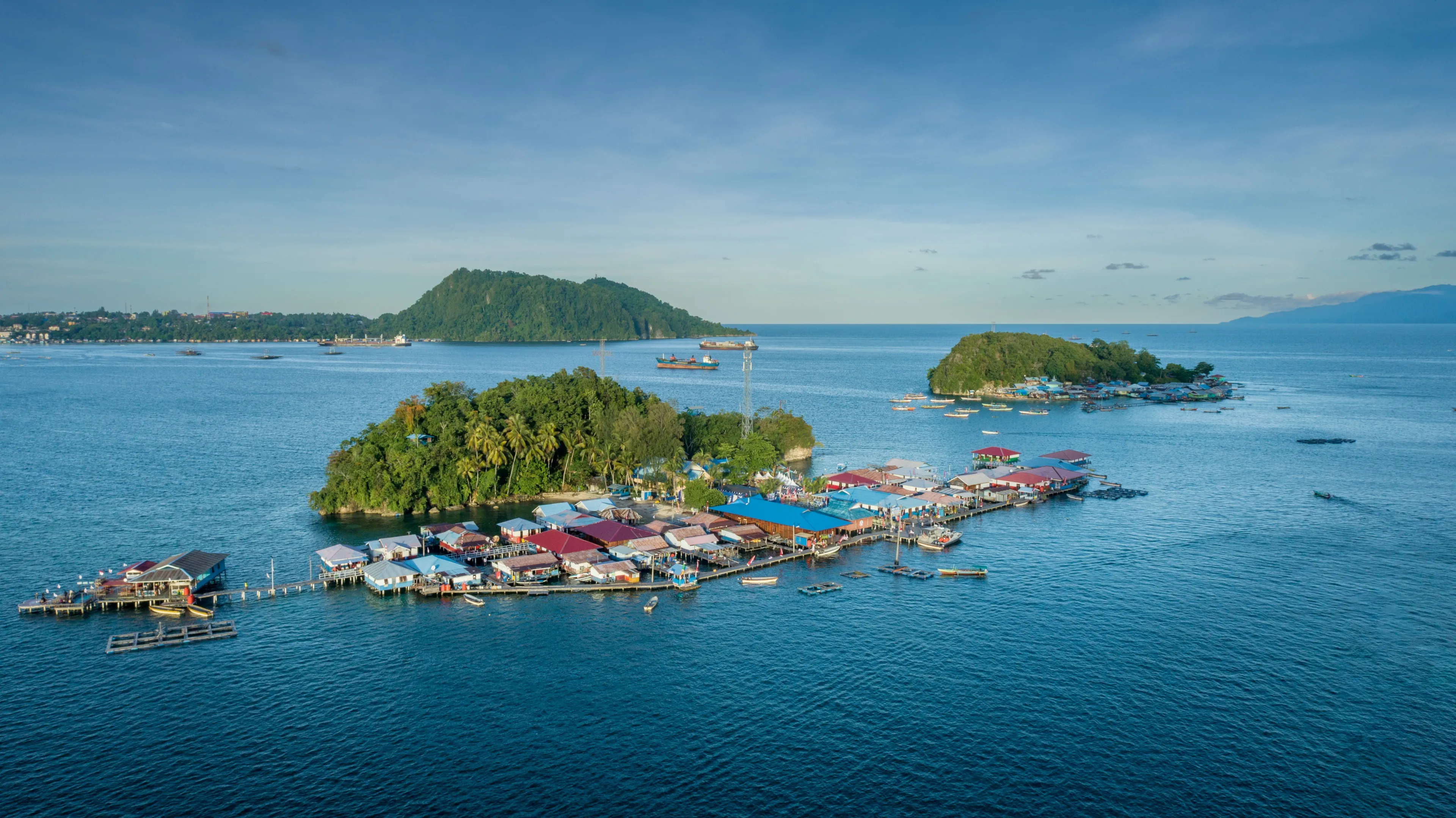 A fishing village on small islands in Jayapura, Papua, Indonesia. The village is above the sea, under clear and cloudy skies, with boats and fishing gear around