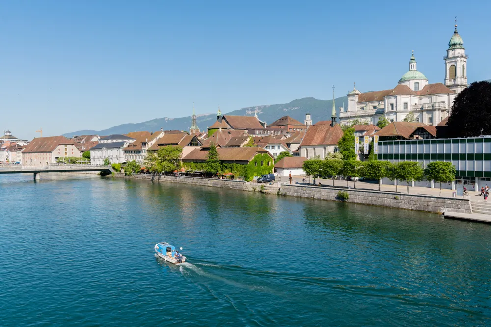 Solothurn, SO / Switzerland - 2 June 2019: city of Solothurn with the river Aare panorama cityscape view of the old town and a fishing boat heading upstream